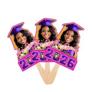 May include: Three graduation fan favors featuring a smiling woman wearing a purple graduation cap with gold tassels. The fans have the text "You Did It Shantel 2026" in pink and purple.
