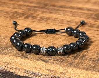 May include: A black beaded bracelet with silver accents. The bracelet is made of round beads and has a sliding knot closure.