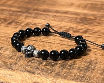May include: Black beaded bracelet with a silver skull charm. The bracelet is adjustable with a black cord.