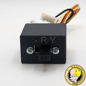 May include: A black electronic switch with the letters "-RY" printed on the front. The switch has a toggle and is secured with two screws. Wires with white, yellow, red, and black insulation extend from the top. A logo with a cartoon character is in the bottom right corner.