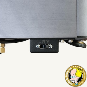 May include: Close-up of a black switch with the text "-RY" and a toggle switch. The switch is mounted on a larger, metallic gray component. The image is well-lit, with a neutral background. The switch appears to be part of a larger electronic device.