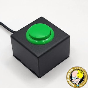 May include: A black square button with a large, bright green button on top. The button is connected to a black wire. The button is likely for electronics or industrial use.