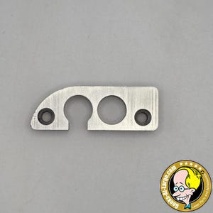 May include: A silver-colored metal bracket with two circular holes and a keyhole-shaped cutout. Two smaller holes with black inserts are on the ends. The bracket is on a gray background. The image includes a logo in the bottom right corner.