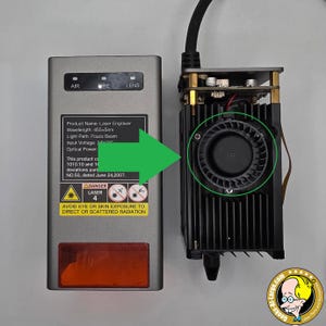 Peut inclure: Un graveur laser avec un boîtier noir et argenté, comprenant un ventilateur et une étiquette d'avertissement. Le nom du produit, la longueur d'onde et d'autres spécifications sont visibles. L'image comprend également une flèche verte pointant vers le ventilateur.