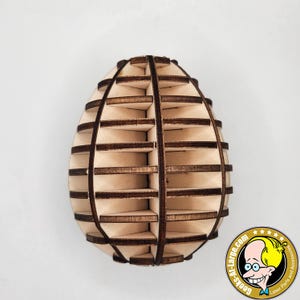 Könnte beinhalten: Ein hölzernes, eiförmiges Dekorationsstück mit einem geschichteten Design. Der Artikel besteht aus hellfarbenem Holz mit dunkleren braunen Kanten, wodurch ein Kontrast entsteht. Das Design weist horizontale Lamellen auf, die ihm eine einzigartige, offene Struktur verleihen. Der Artikel ist wahrscheinlich ein dekoratives Stück.