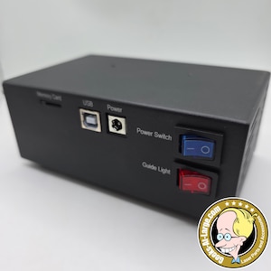 May include: Black rectangular electronic device with USB and power ports, and a memory card slot. It has a blue power switch and a red guide light switch. The text "Power Switch" and "Guide Light" are visible.