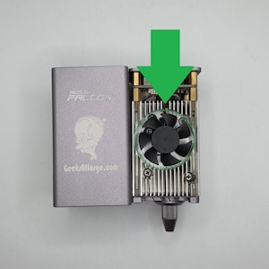 以下が含まれることがあります： 「CREALITY FALCON」の文字とメガネをかけた人物の漫画の画像が描かれた、銀色のレーザー彫刻機。GeekAtLarge.comのウェブサイトも表示されています。このデバイスにはファンと金属部品が備わっています。