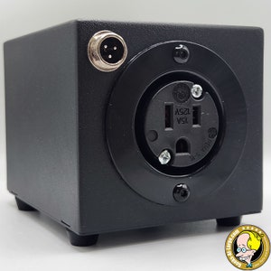 May include: A black electrical box with a NEMA 5-15 outlet and a 3-pin connector. The outlet is rated for 125V and 15A. The box has four small feet and a circular black trim around the outlet.