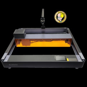 Pode incluir: Uma máquina de gravação a laser preta e cinza com uma capa protetora laranja. A máquina tem uma tela pequena e a marca "ELEGOO" é visível. Um logotipo de desenho animado está no canto superior direito.