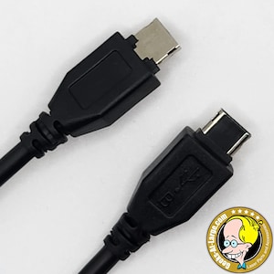 Könnte beinhalten: Zwei schwarze USB-C-zu-USB-B-Kabel. Die Stecker sind rechteckig mit silberfarbenen Metallkontakten. Die Kabel sind schwarz und flexibel. Das Bild ist vor einem weißen Hintergrund.