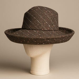 May include: A brown hat with a wide brim and a structured crown. The hat features a diagonal striped pattern with white and pink flecks. The hat is displayed on a mannequin head.