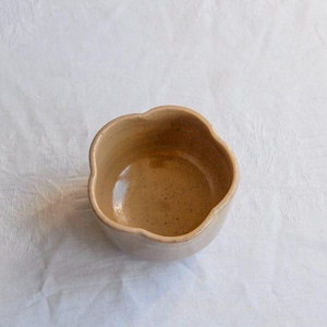 Könnte beinhalten: Eine kleine, beige Keramikschale mit einem einzigartigen, gewellten Rand. Das Innere hat ein gesprenkeltes Aussehen, und die Schale steht auf einer weißen Oberfläche. Diese handgefertigte Schale ist ideal zum Servieren kleiner Portionen.