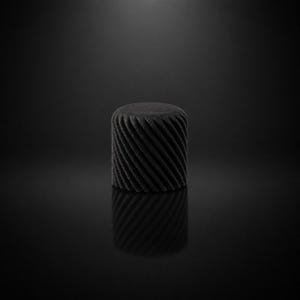 Könnte beinhalten: Ein zylindrischer, schwarzer Hocker mit einem strukturierten, spiralförmigen Design. Der Hocker besteht aus einem dunklen, matten Material und reflektiert das Licht, wodurch ein Spiegeleffekt auf der darunter liegenden Oberfläche entsteht.
