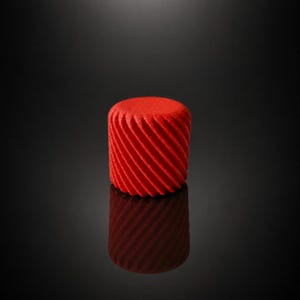 Könnte beinhalten: Ein leuchtend rotes, zylindrisches Objekt mit einem strukturierten, diagonal gestreiften Muster. Das Objekt spiegelt sich auf einer dunklen, glänzenden Oberfläche, wodurch ein symmetrisches Bild entsteht. Das Design ist modern und auffällig.