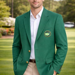 Könnte beinhalten: Grüner Blazer mit goldenen Knöpfen und einem Aufnäher mit einem Golfplatzlogo. Der Blazer wird über einem weißen Hemd und mit einer beigefarbenen Hose getragen. Die Person steht auf einem grünen Rasen.