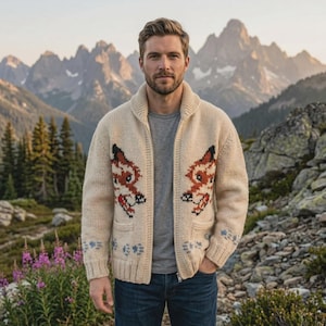 Puede incluir: Cárdigan crema con cremallera y diseños de zorro en la parte delantera. El suéter tiene cuello chal, dos bolsillos y detalles florales azules. El fondo presenta una cordillera y árboles.