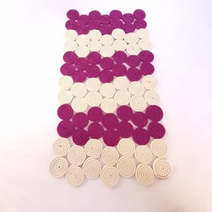 May include: A white and pink woven rug made of coiled rope. The rug is made up of rows of circles, with alternating colours of white and pink.