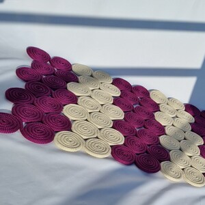 May include: A decorative rug made of woven circles in shades of purple and cream. The circles are arranged in a repeating pattern, creating a unique and stylish design.