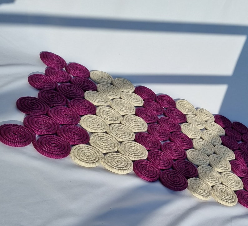 May include: A decorative rug made of woven circles in shades of purple and cream. The circles are arranged in a repeating pattern, creating a unique and stylish design.