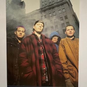 May include: Poster featuring the band Offspring, with four members posing in front of a city building. The poster has a dark color palette, with the band members wearing jackets and hoodies. The text "PHOTO FEATURE: OFFSPRING PUBLISHED BY ANABAS" is at the bottom.