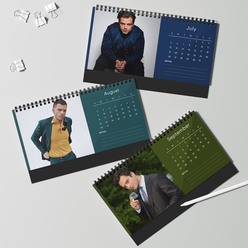 May include: A collection of spiral-bound desk calendars featuring photographs of a person. Each calendar displays a different month, with the months of July, August, and September visible. The calendars have a black base and a white spiral binding.