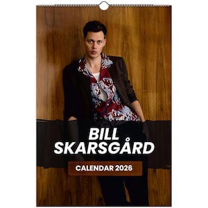 May include: A wall calendar featuring a person in a dark blazer over a patterned shirt. The calendar has the text "BILL SKARSGÅRD" in large white letters, with "CALENDAR 2026" below. The background is a wooden wall.