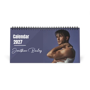 May include: A horizontal spiral-bound desk calendar for the year 2027 featuring the text Calendar 2027 and the name Jonathan Bailey in white script. The right side displays a portrait of a person with dark hair wearing a white tank top.