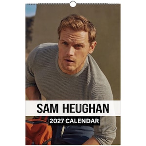 May include: A 2027 wall calendar featuring a portrait of Sam Heughan. The image shows a person with light brown hair wearing a grey waffle-knit long-sleeve shirt. The text SAM HEUGHAN and 2027 CALENDAR is printed in black on a white banner.