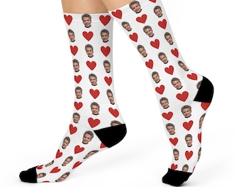 Peut inclure: Chaussettes blanches avec un motif répété de coeurs rouges et du visage d'une personne. Les chaussettes ont des talons et des orteils noirs. Les chaussettes sont portées sur les jambes d'une personne.
