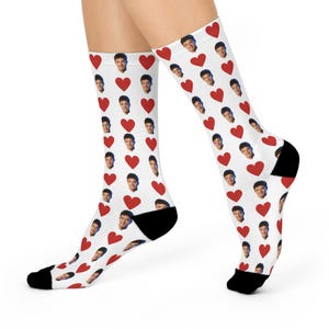May include: White socks with a pattern of red hearts and faces. The socks have black heels and toes. The faces are of a person with dark hair and a mustache.