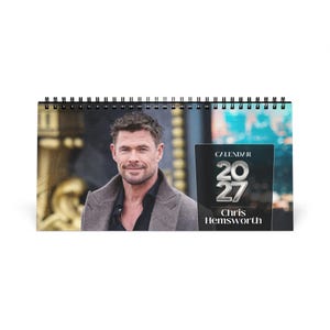 May include: A horizontal spiral-bound wall calendar featuring a portrait of Chris Hemsworth wearing a grey coat over a black shirt. The text on the right side reads CALENDAR 2027 and Chris Hemsworth in white and silver metallic lettering.