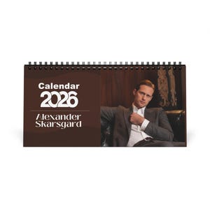 May include: A spiral-bound desk calendar for 2026 featuring actor Alexander Skarsgard. The cover has the word "Calendar" above the year "2026" and the name "Alexander Skarsgard" in white text on a brown background. The right side shows a photo of Skarsgard.