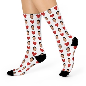 May include: White socks with a pattern of red hearts and faces. The socks have black heels and toes. The socks are knee-high.