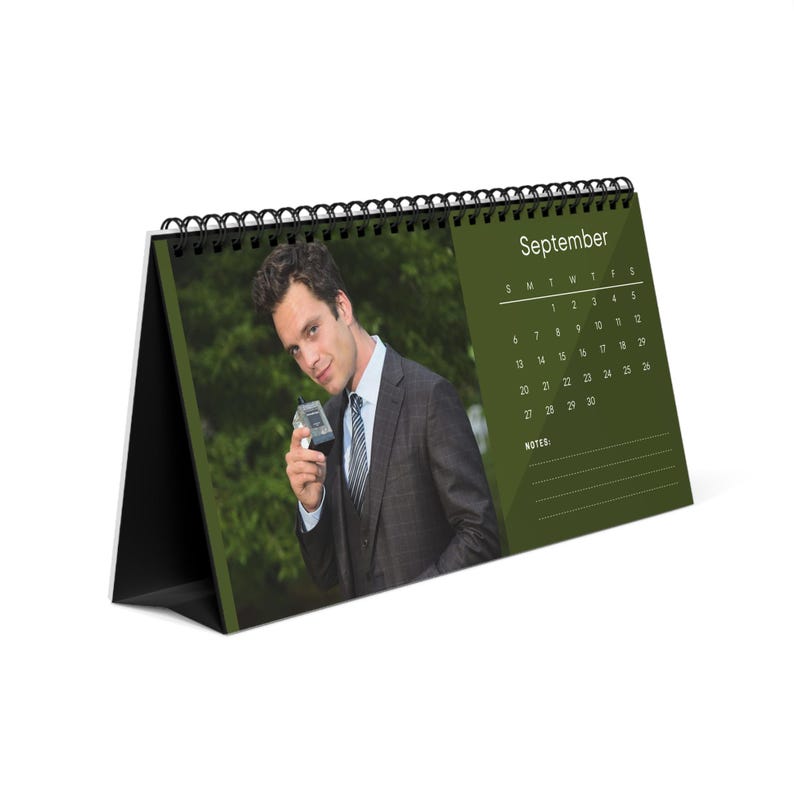 May include: A desk calendar for September featuring a man in a suit holding a device. The calendar has a green background with the month and dates printed in white. The calendar is held together with a black wire binding.