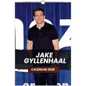 Puede incluir: Calendario con Jake Gyllenhaal. Presenta una foto de Jake Gyllenhaal con una camisa polo negra. El texto "JAKE GYLLENHAAL" está impreso en blanco y "CALENDAR 2026" en marrón.