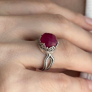 May include: A silver ring with a large, faceted, red gemstone set in a filigree design.