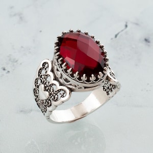 May include: A silver ring featuring a large, oval-shaped, red gemstone set in a filigree design.