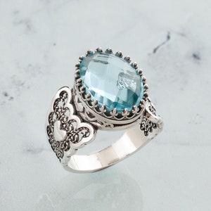 May include: A silver ring with a large, oval-shaped, light blue gemstone set in a filigree design.