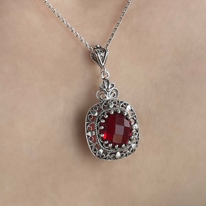 Peut inclure: Un collier en argent avec un pendentif en pierre rouge. Le pendentif est entouré de filigranes d'argent complexes.