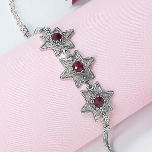 May include: A silver bracelet with three star-shaped charms, each featuring a red gemstone in the center. The bracelet has a delicate chain design and a lobster clasp closure.