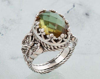 May include: A silver ring with a large, oval-shaped green and brown gemstone. The ring has a detailed design with a butterfly on one side.