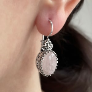May include: Silver dangle earrings featuring a pink rose quartz stone. The earrings have a delicate floral design.