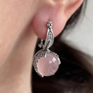 Puede incluir: Pendientes de plata con un delicado diseño de filigrana y una piedra de cuarzo rosa.