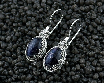 Puede incluir: Un par de pendientes colgantes de plata con gotas ovaladas de piedra azul. Los pendientes tienen un delicado diseño floral.
