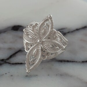 May include: A silver filigree ring with a flower design. The ring is delicate and intricate, with a floral pattern that is reminiscent of a vintage style.