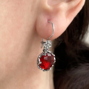May include: Silver dangle earrings with a red gemstone and a floral design.