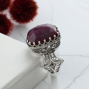 Può includere: Un anello d'argento con un design filigranato decorato e una grande pietra preziosa ovale di colore rosso scuro.