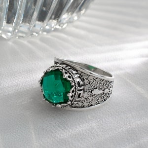 May include: A silver ring with an ornate design and a large, round, green gemstone.