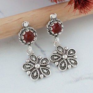 May include: Silver dangle earrings with a red gemstone and a floral design.