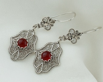 May include: A pair of silver filigree earrings featuring red carnelian gemstones. The earrings have a delicate, intricate design and are perfect for adding a touch of elegance to any outfit.